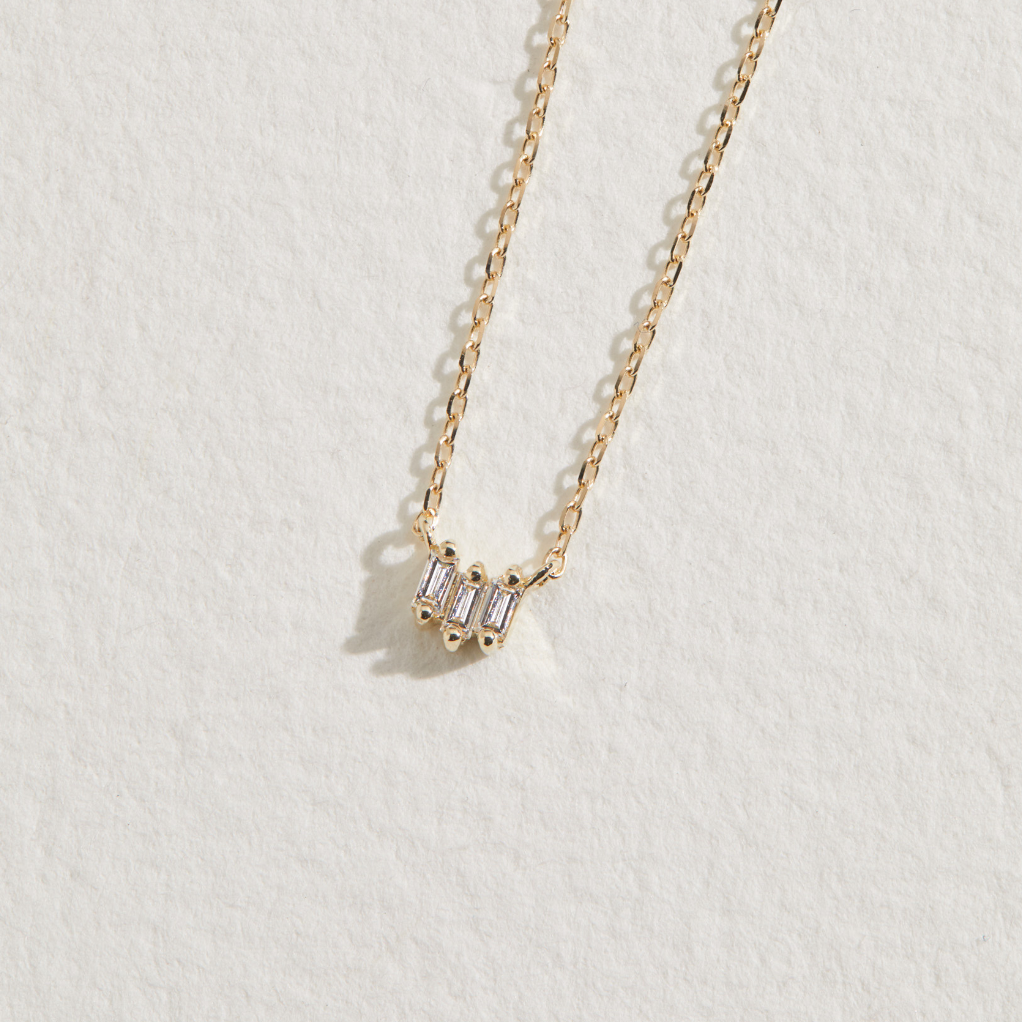 Gold triple baguette diamond necklace on a paper surface