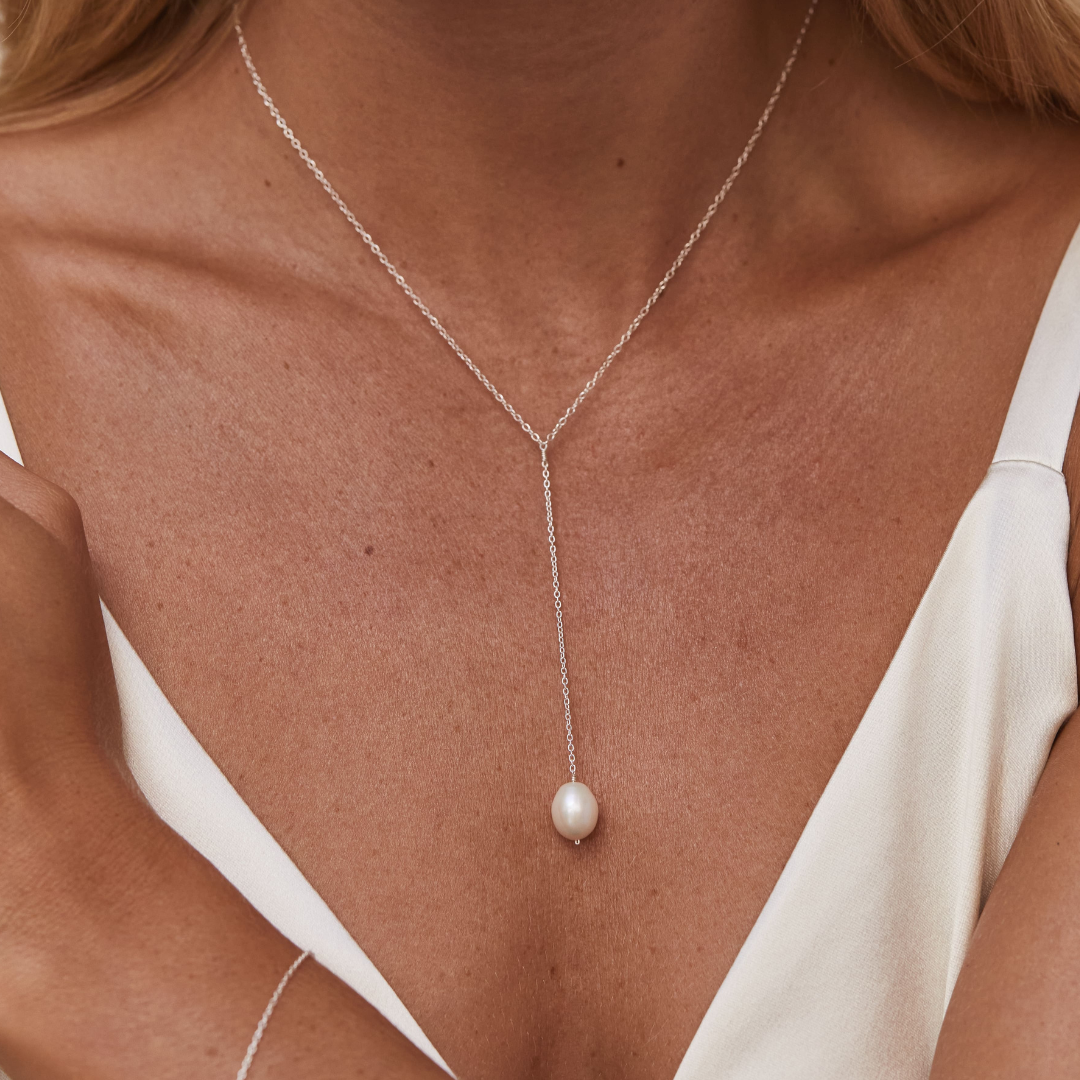 Gold large pearl lariat necklace around the neck of a blonde woman wearing a white top