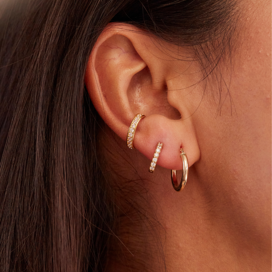 Close up of gold thick diamond style ear cuff in one ear paired with another gold cuff and a gold huggie hoop earring in her ear