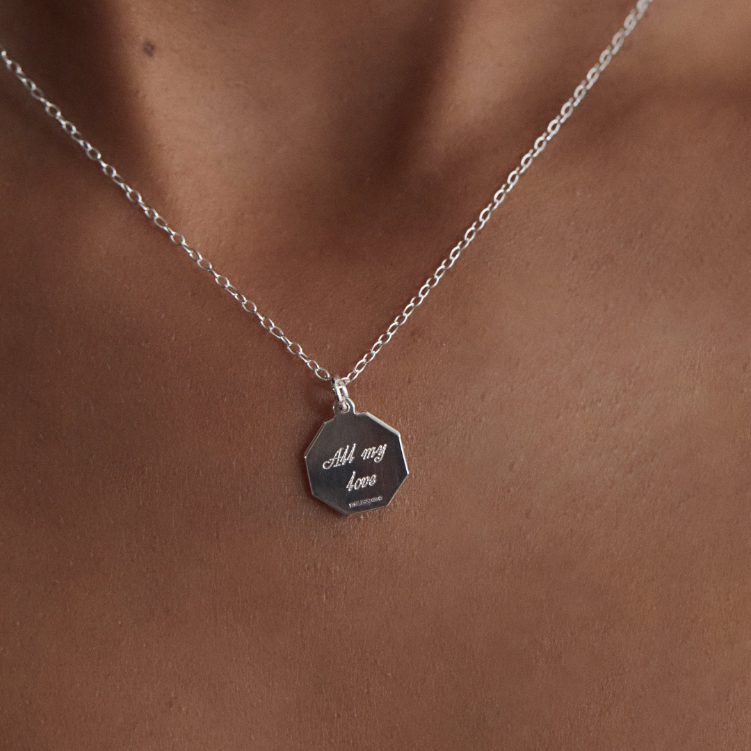 Back of silver small octagonal st christopher necklace with a 'AM my love' engraved on it