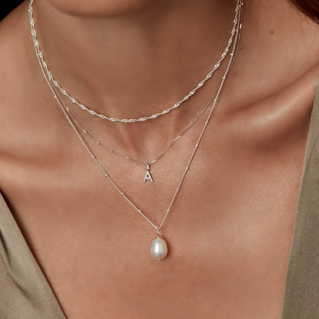 Silver twisted rope chain necklace around a neck layered with a silver satellite pearl necklace and a silver initial charm necklace 'A'