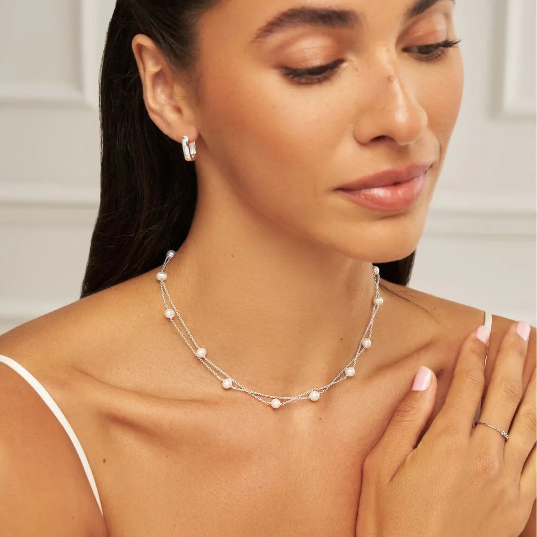 Model looking down wearing small silver squared hoop earrings 