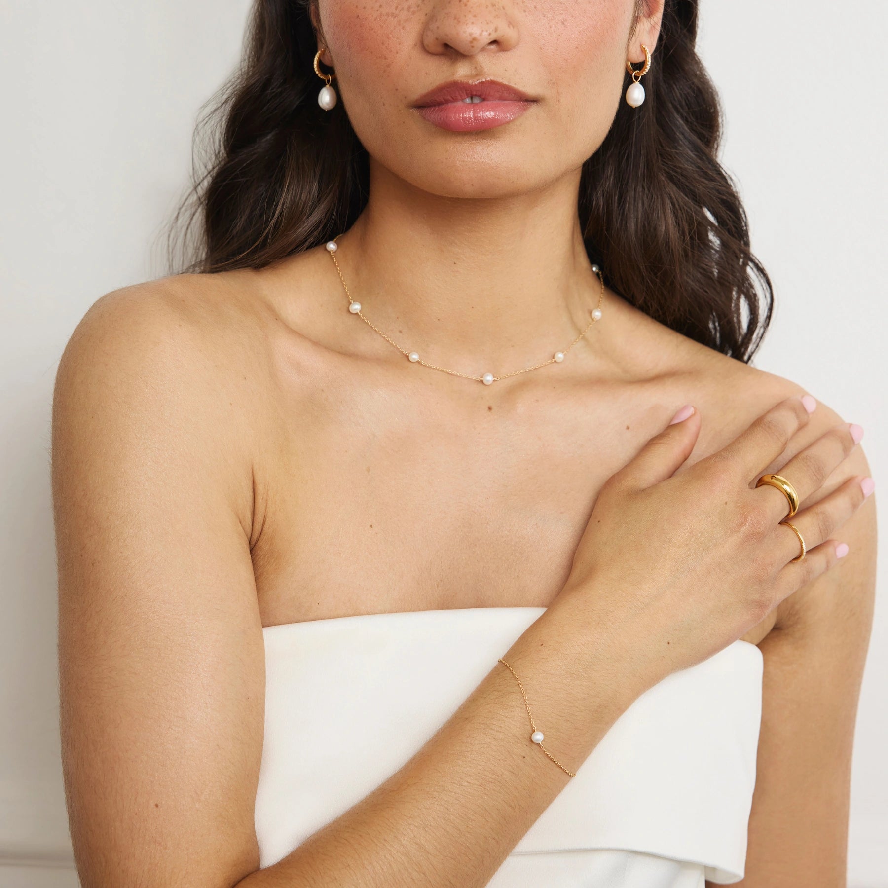 Woman wearing a delicate pearl choker and bracelet with a plain background