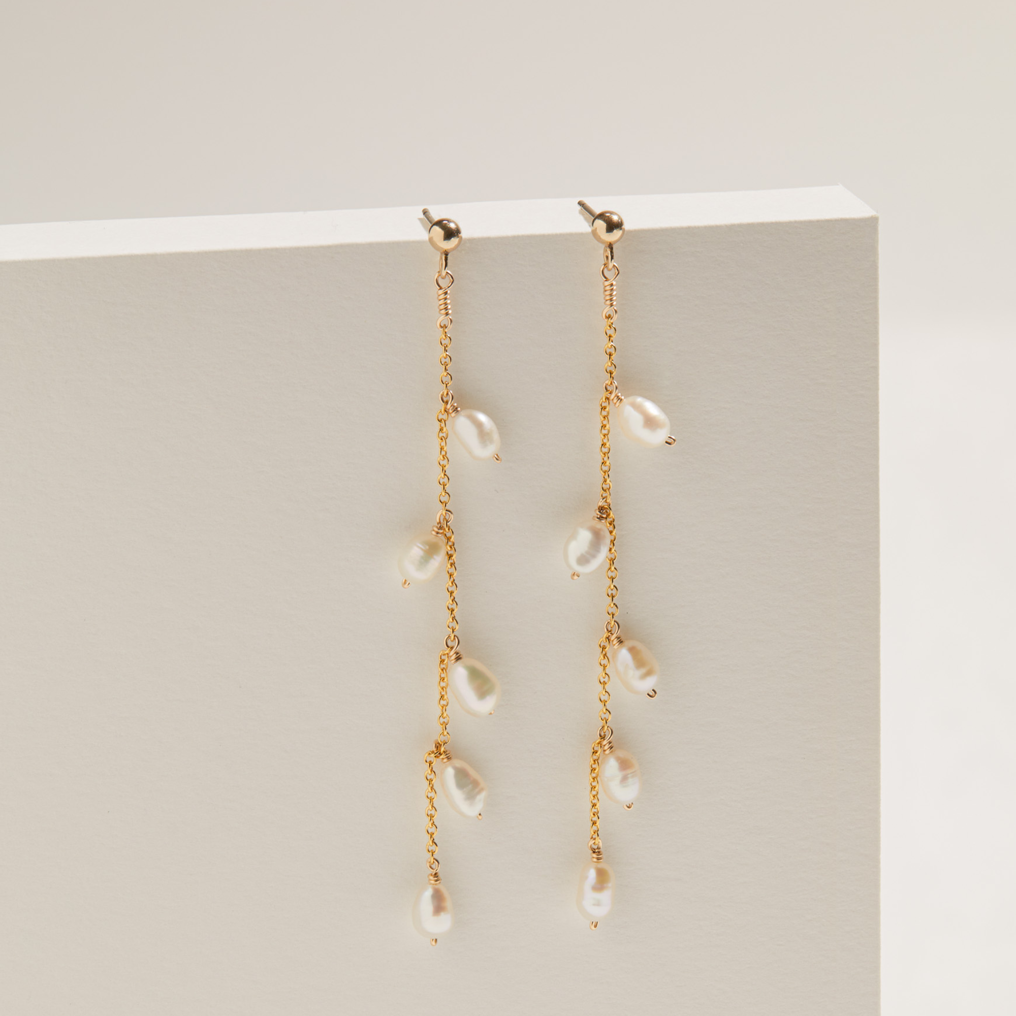 Gold seed pearl drop earrings hanging off a white ledge