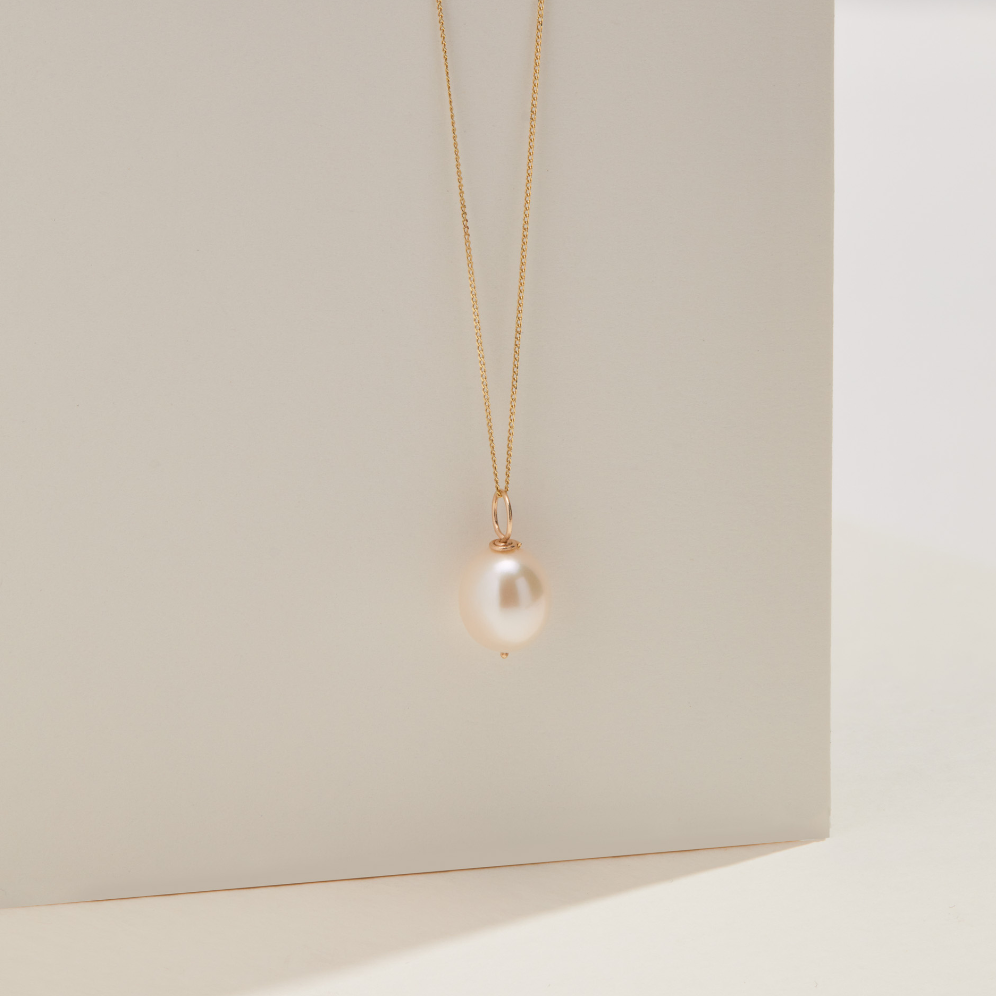 Gold large single pearl necklace infront of a cream board
