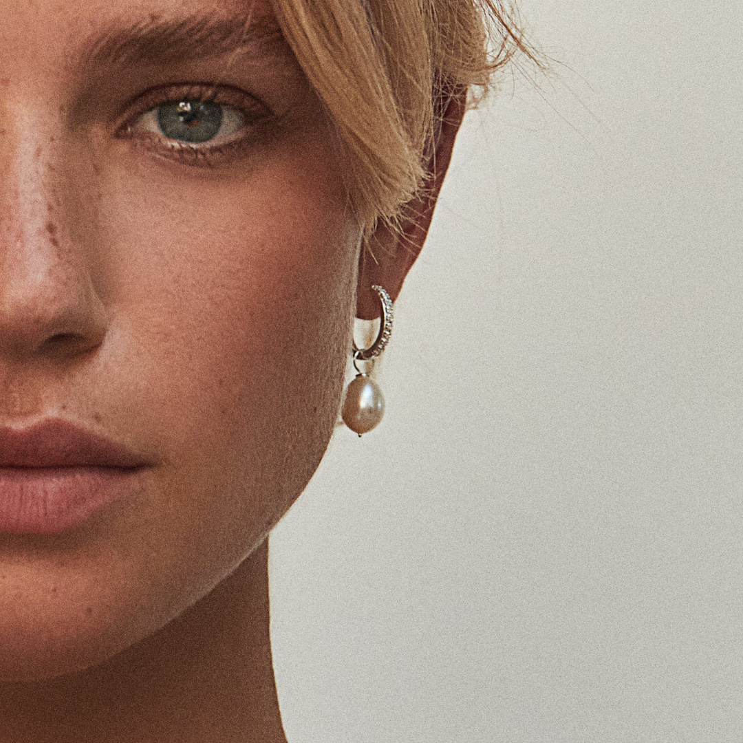 Close up of a blonde woman wearing a silver diamond style large pearl drop hoop earring in her ear lobe