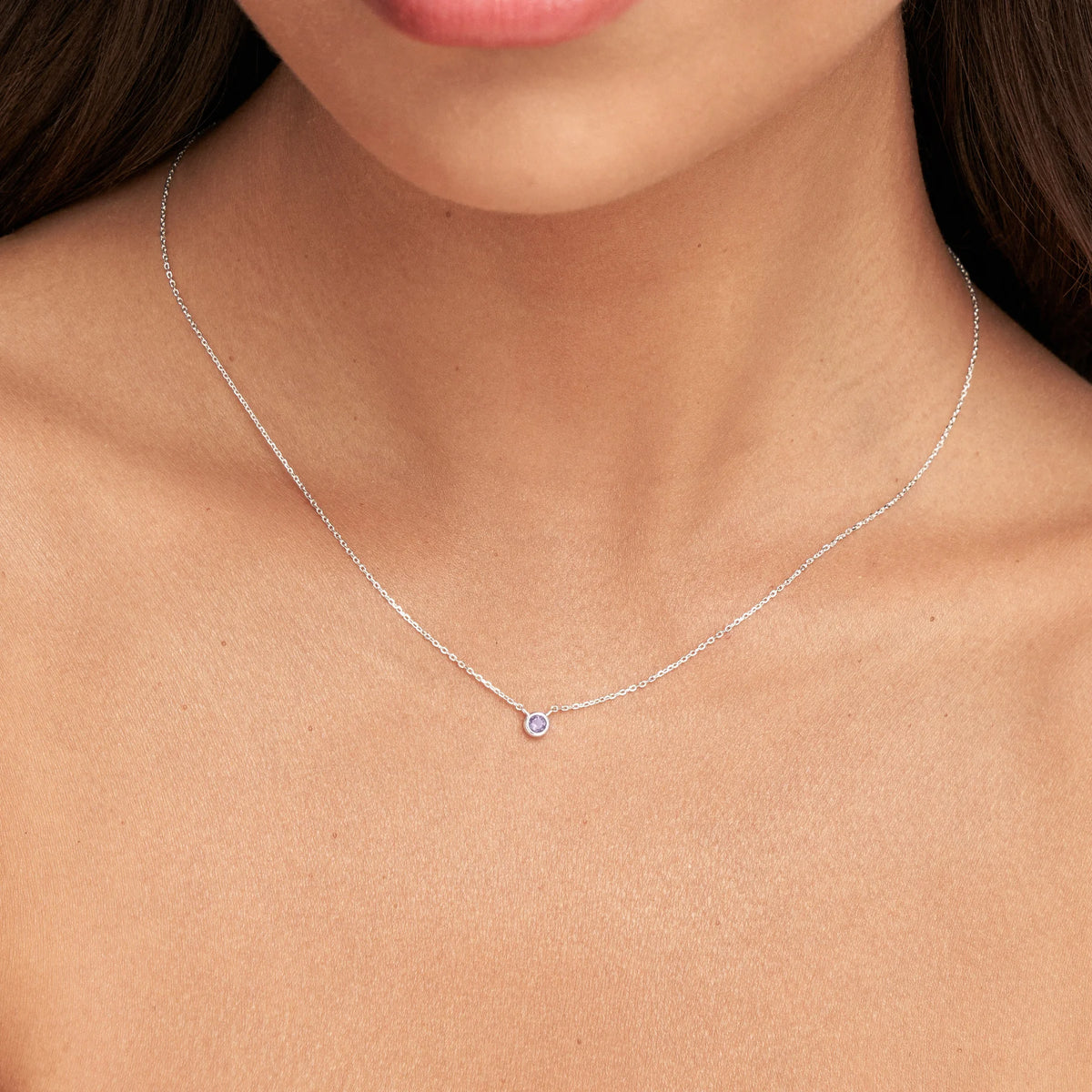 A delicate silver chain necklace with a single small round clear gemstone pendant, shown worn on a model's neck.