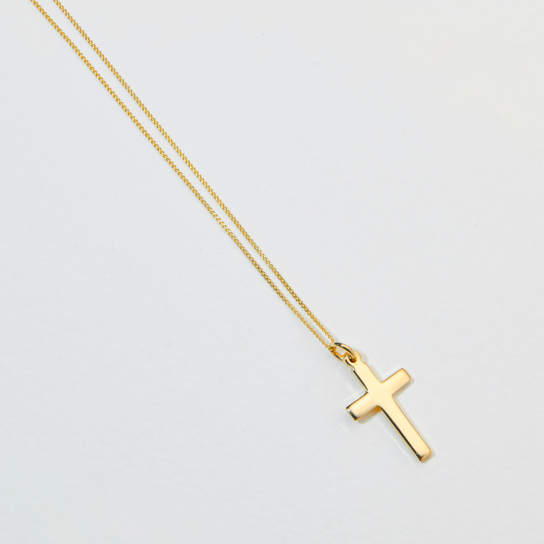 Solid gold cross necklace laying on a white surface 