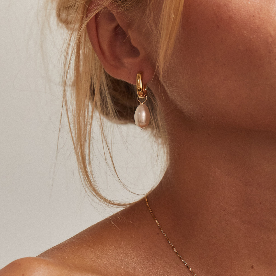 Gold thick squared hoop pearl drop earring in one ear lobe of a blonde woman