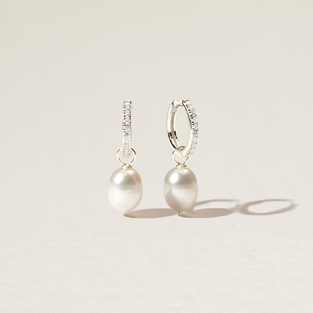 Silver diamond style large pearl drop hoop earrings over a paper backdrop 