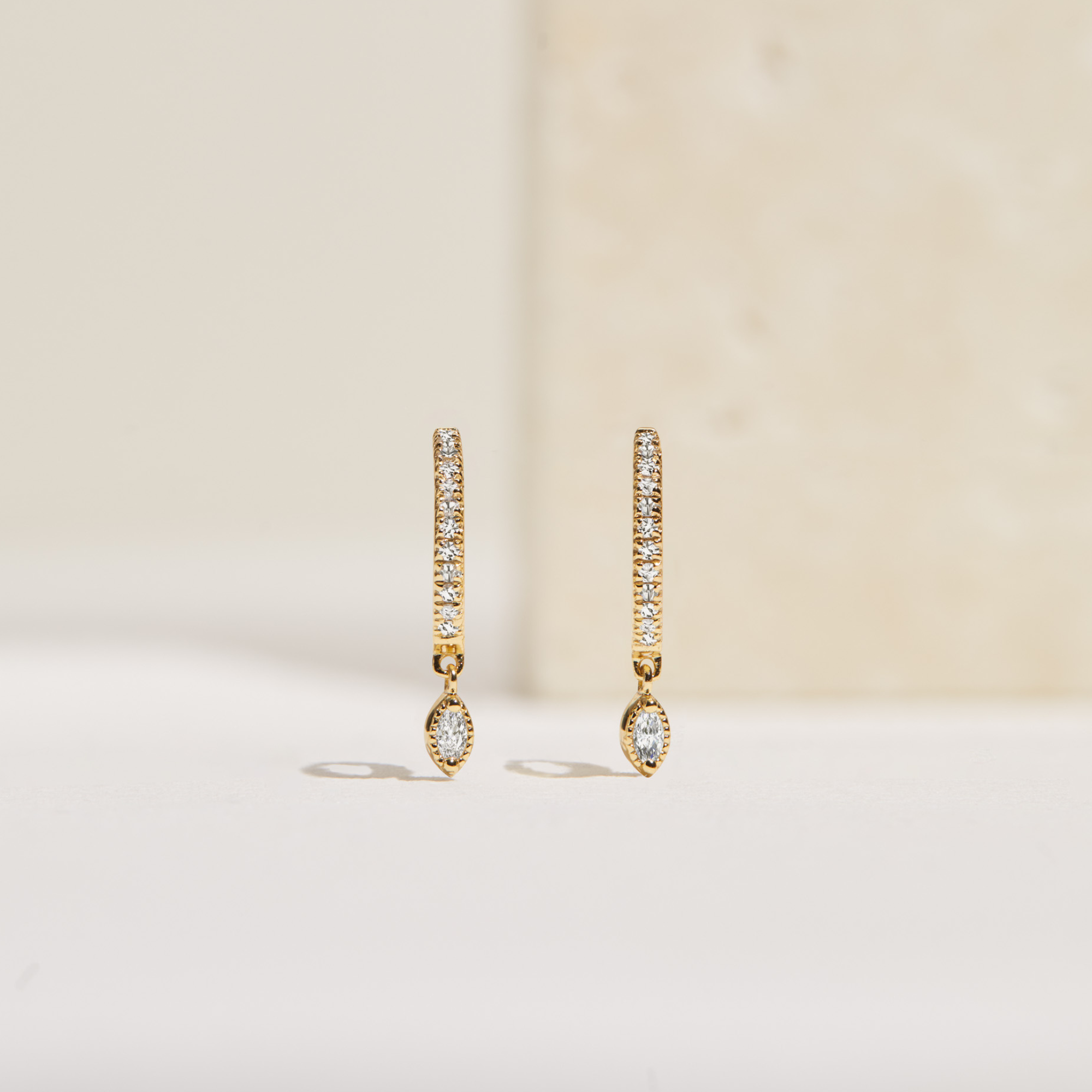 Gold marquise diamond drop hoop earrings over faded cream background
