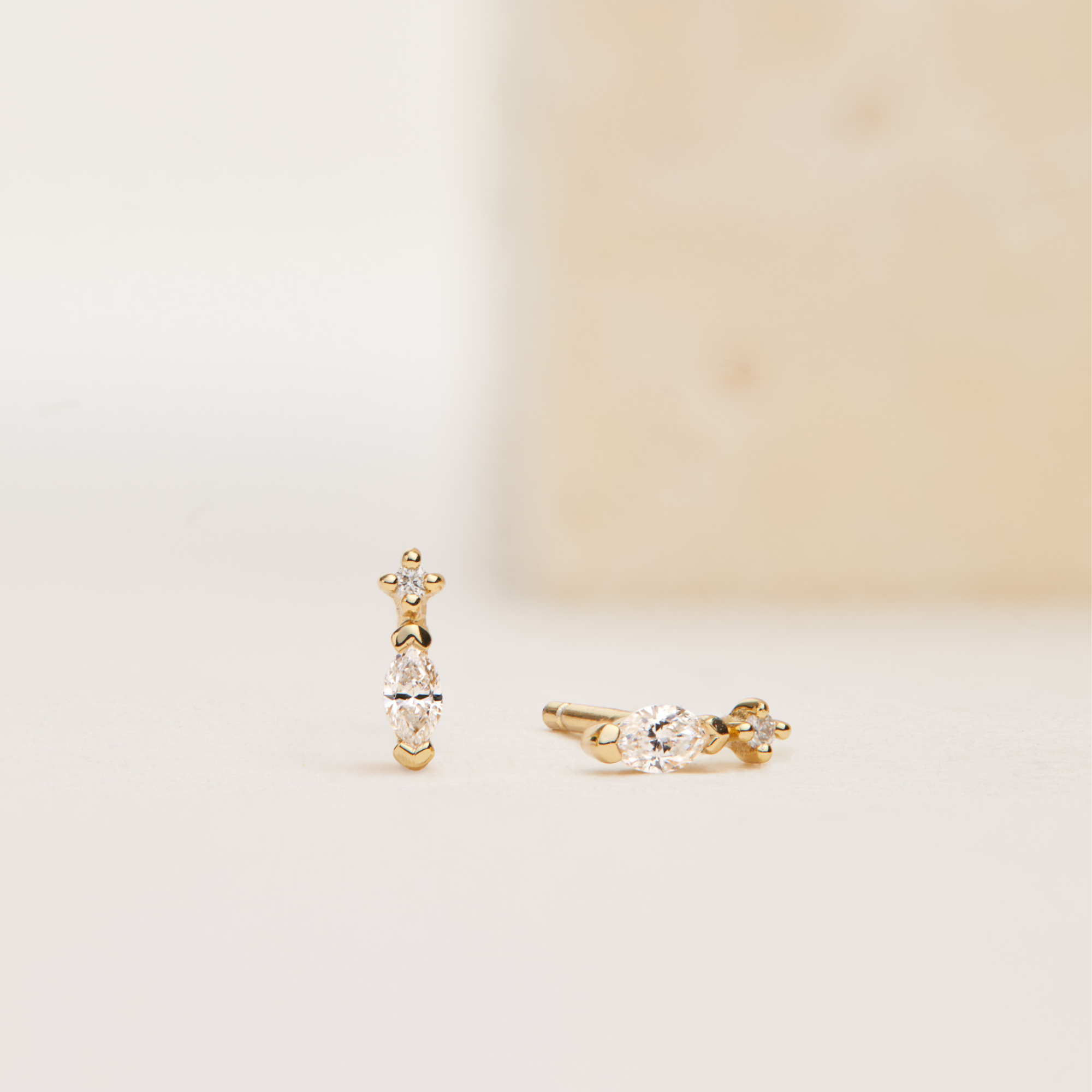 Gold marquise diamond stud earrings one laying down one standing up on a faded cream background