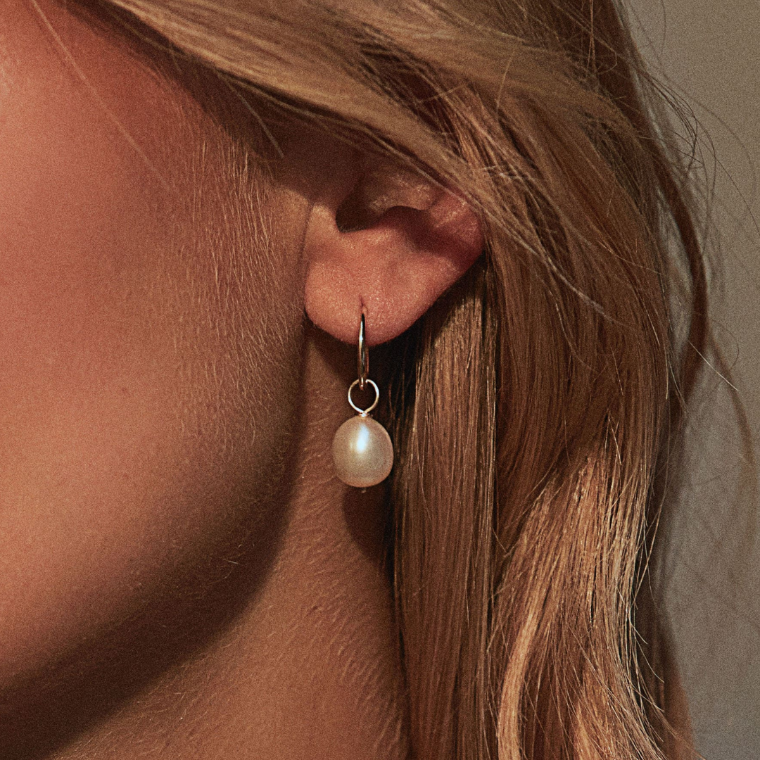 Solid gold large pearl drop hoop earring in an ear lobe of a blonde woman