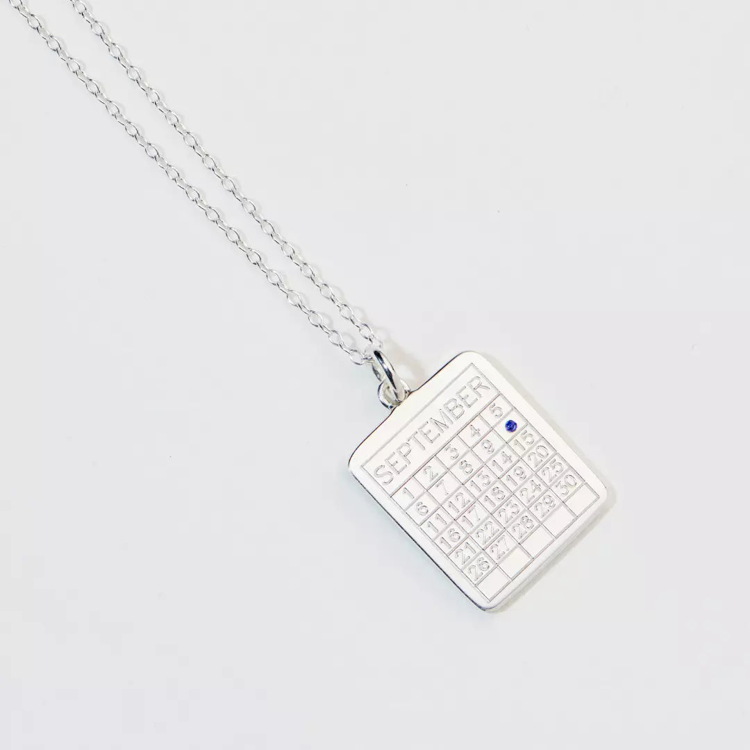 Silver special date calendar necklace 'September' with a blue gemstone on number '10' on a white background