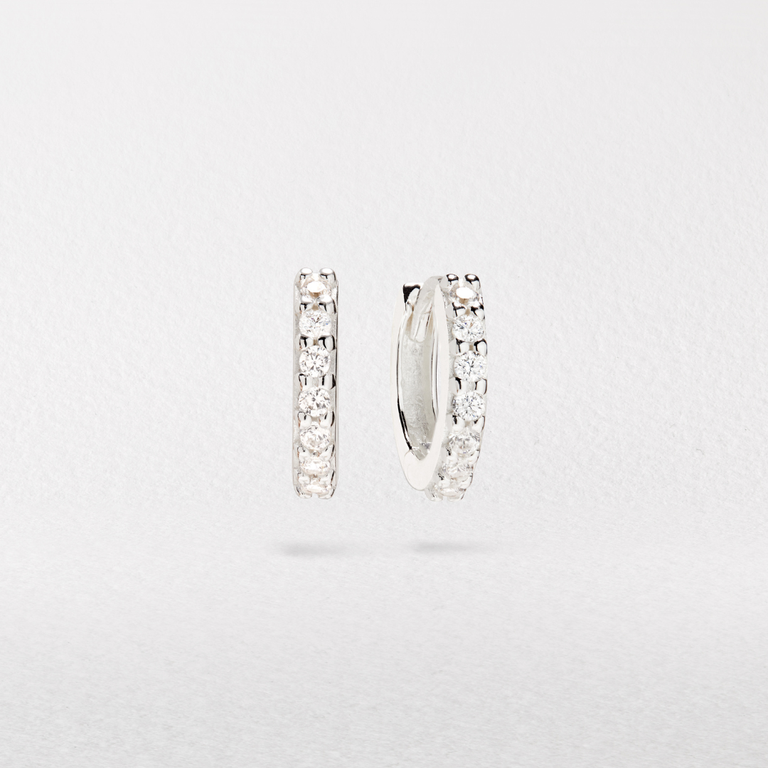 Silver diamond style huggie hoop earrings infront of a white paper background