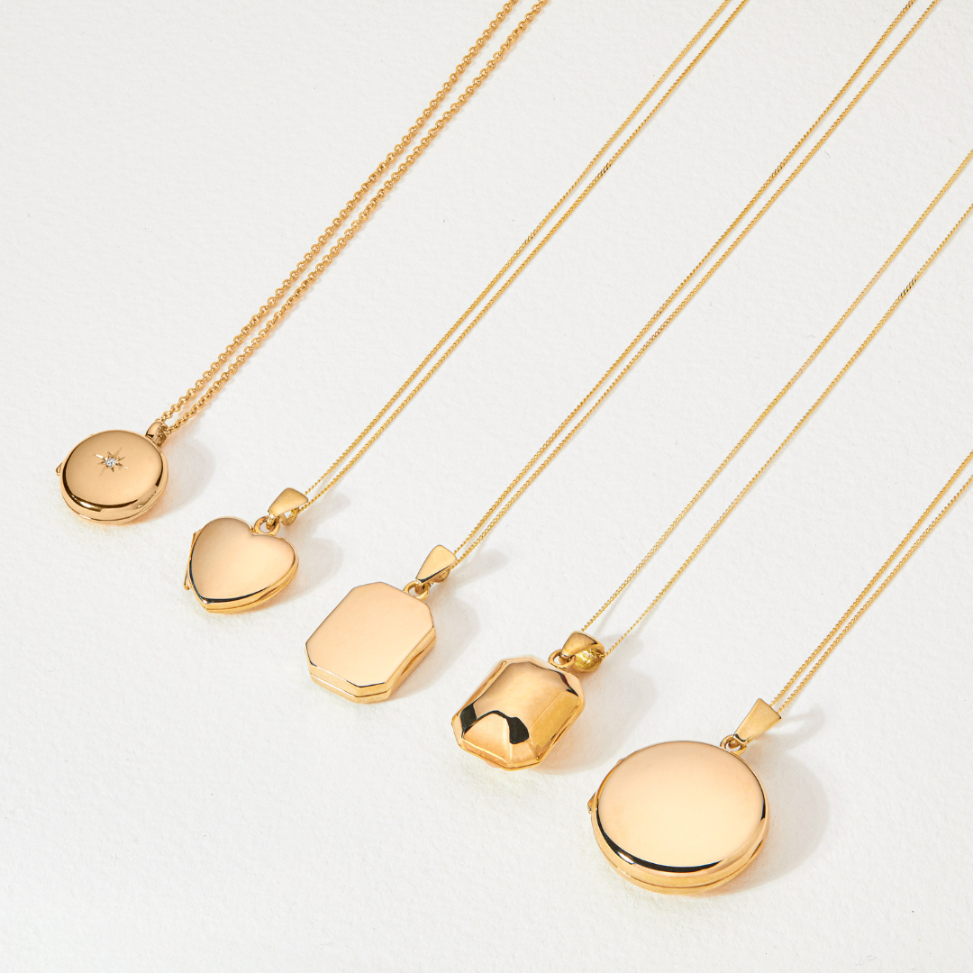 Solid gold ball locket laying on a white surface next to four other different shape gold locket necklaces