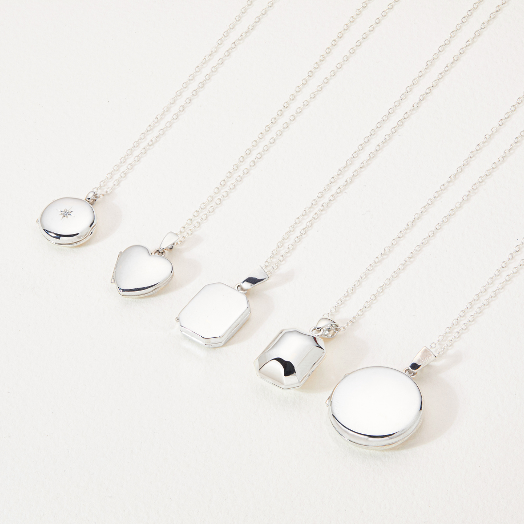 Silver small round diamond locket necklace alongside a silver small heart locket necklace and other silver small locket necklaces