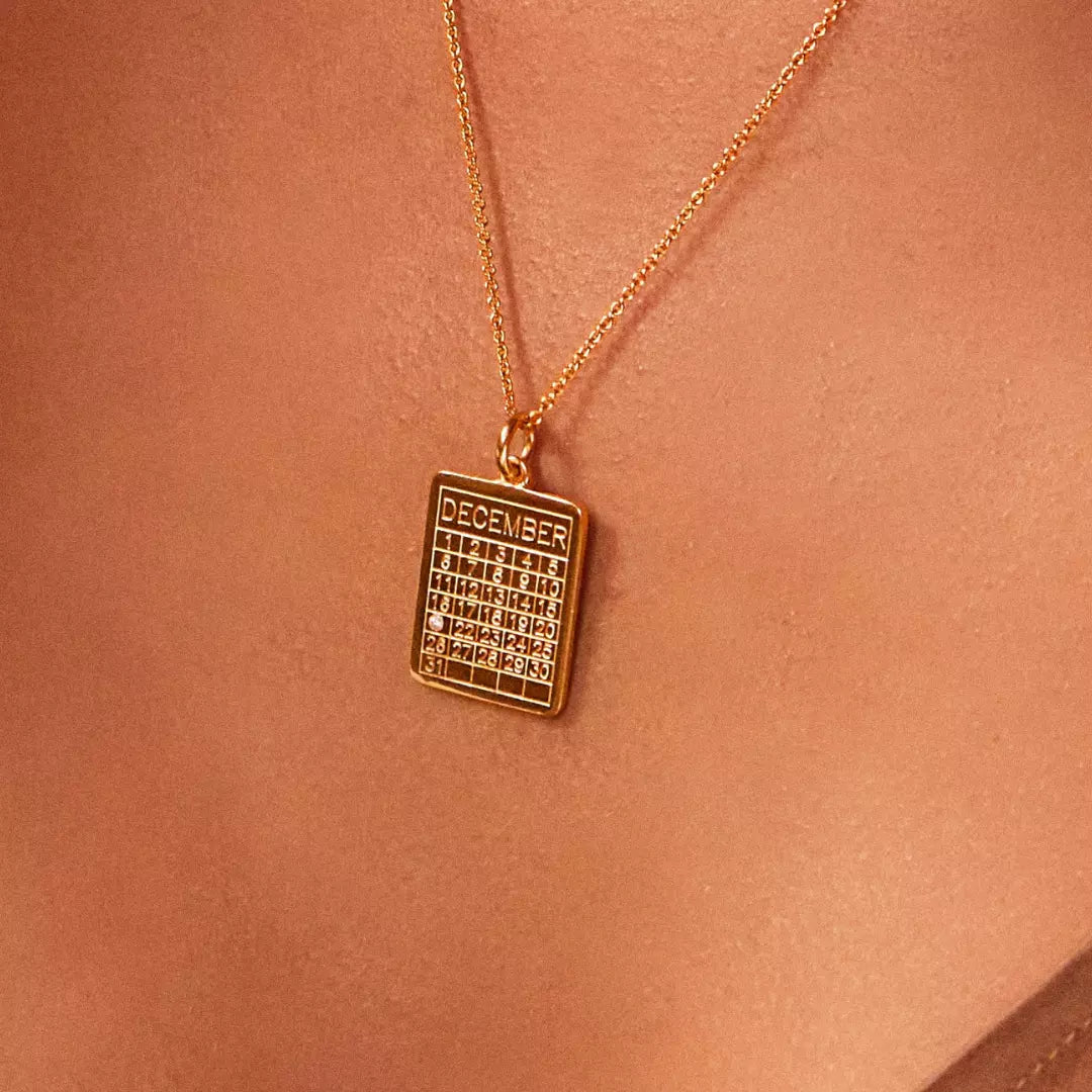 Close up of a gold special date calendar necklace 'December' with the gemstone on number '21',on the chest of a woman wearing a bronze top