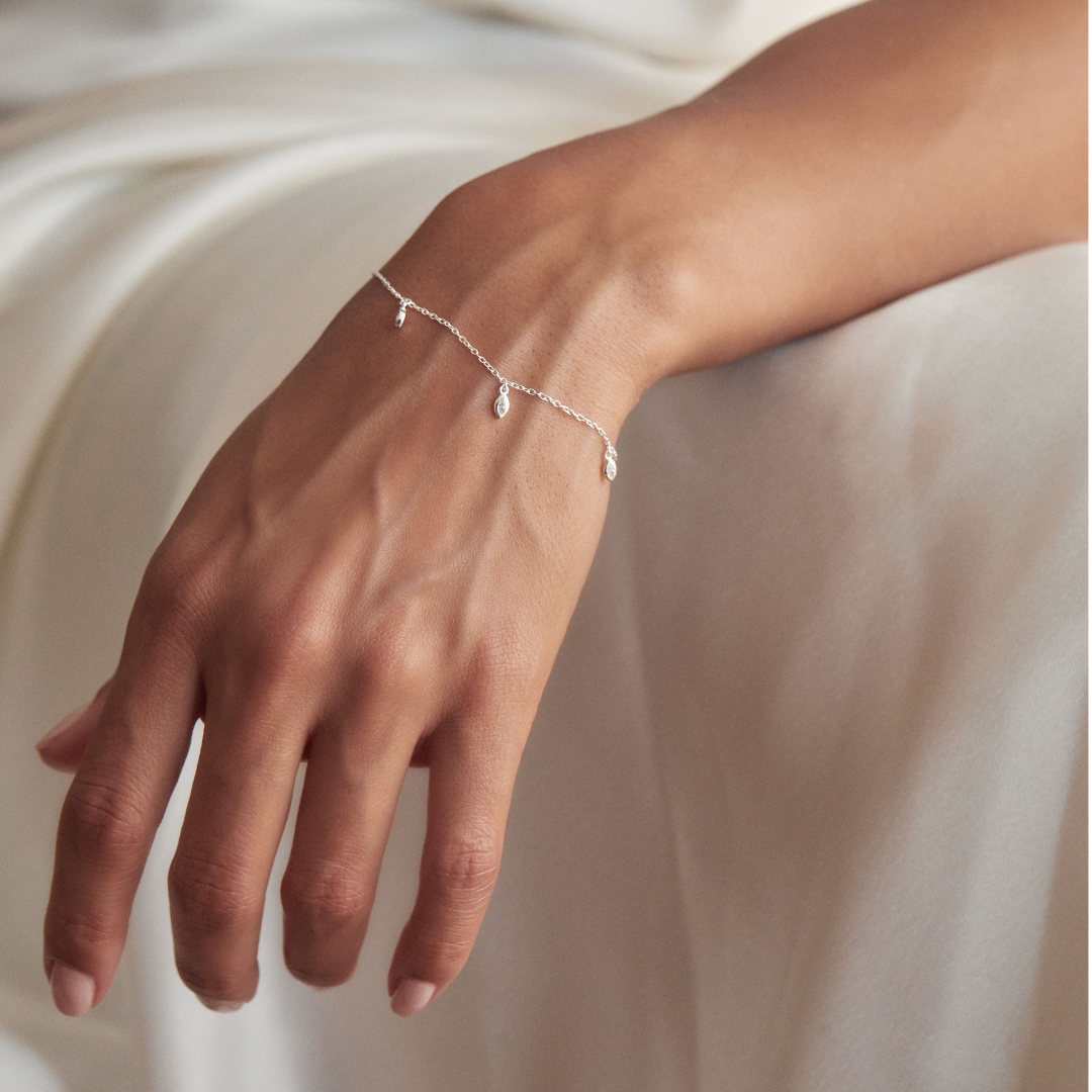 Silver diamond style marquise drop bracelet around a wrist hanging off the edge of a bed