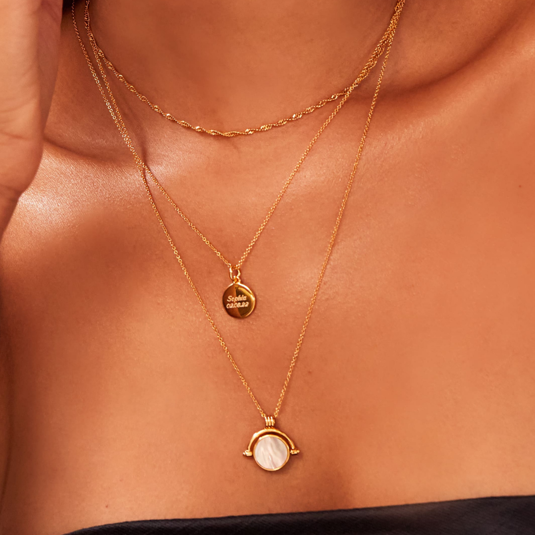 Gold satellite chain necklace layered with a gold twisted rope necklace and a gold small round engraved disc necklace around a neck