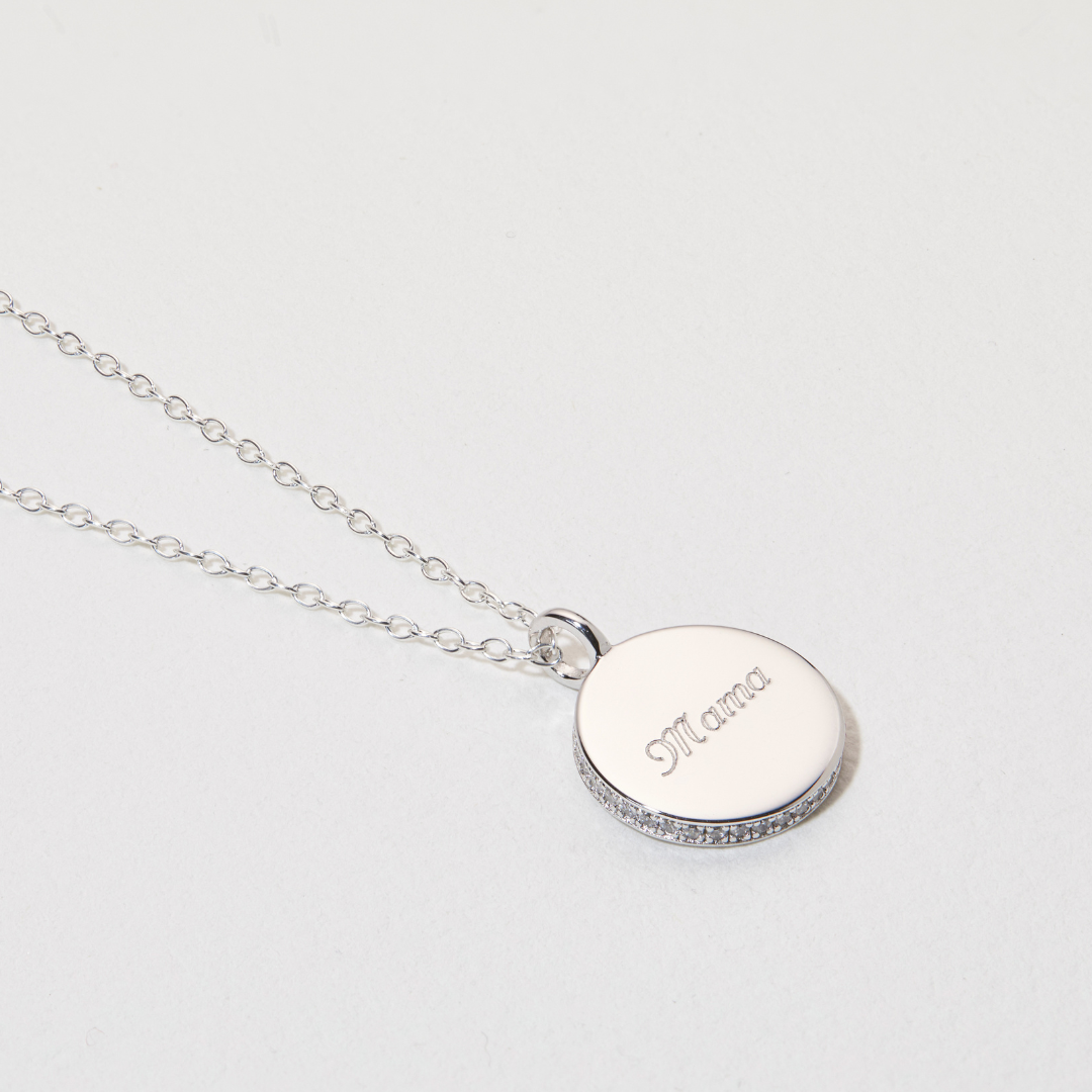 Silver small diamond style disc necklace with the word 'Mama' engraved on a white surface