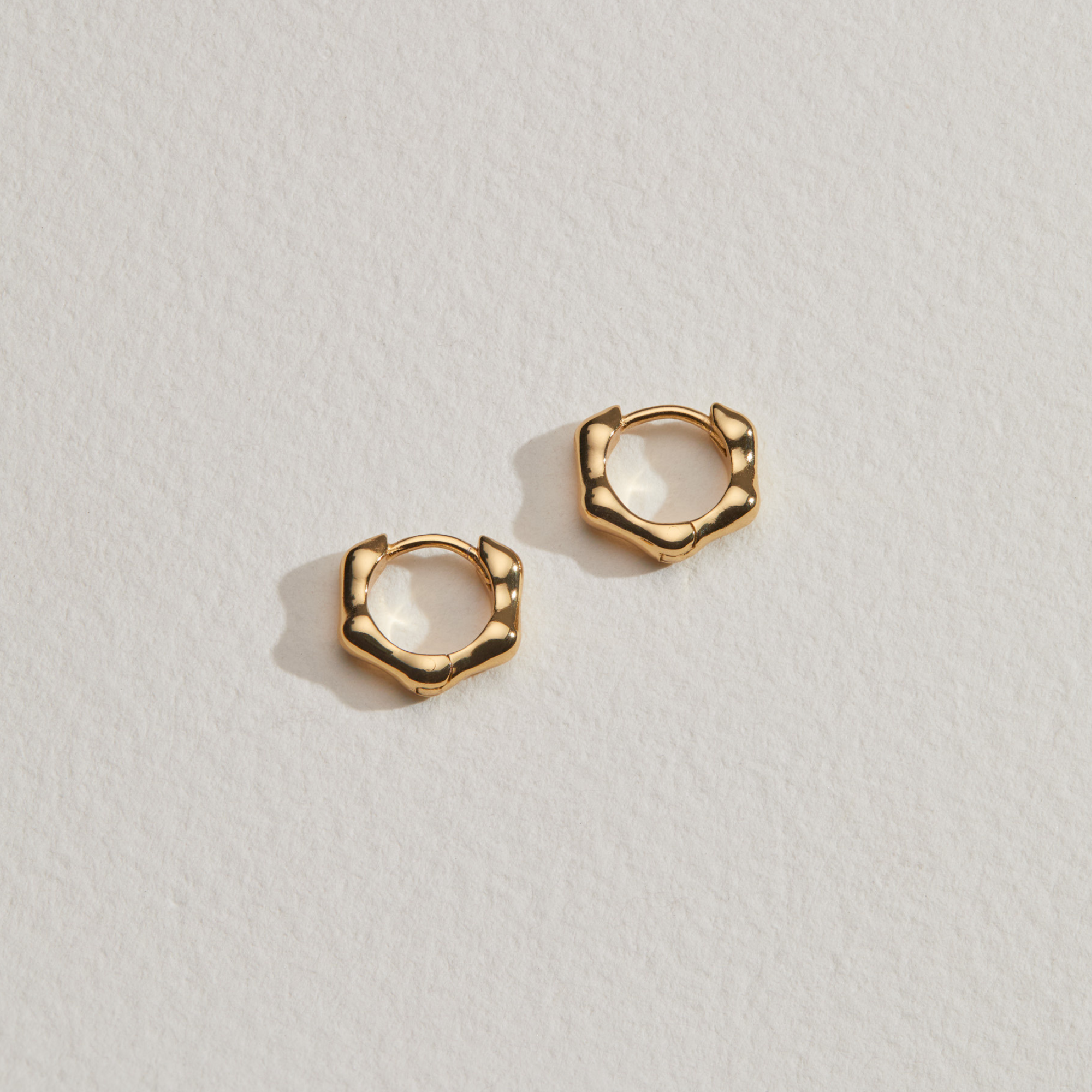 Gold molten huggie hoop earrings on a paper surface