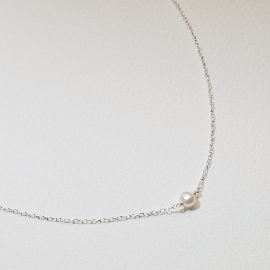 Close up of a silver single pearl choker on a white surface