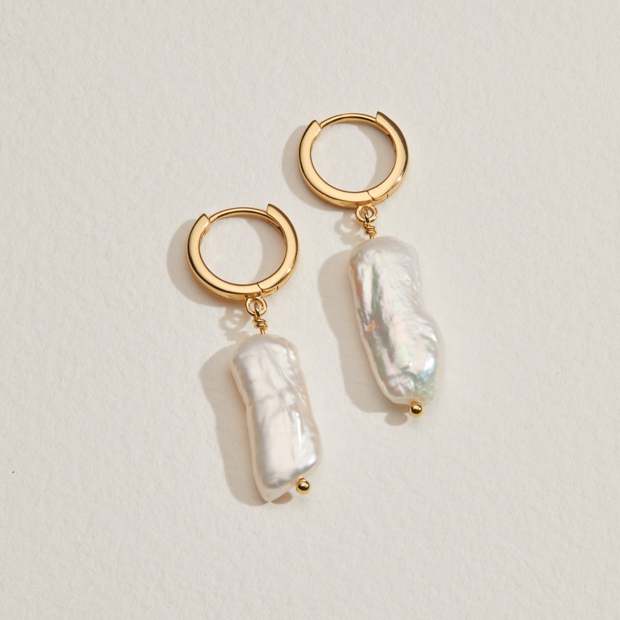 Silver baroque pearl shard hoop earrings on a cream surface