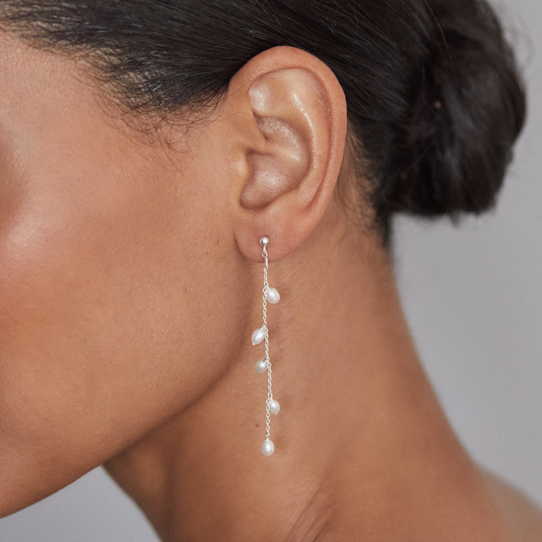 Silver seed pearl drop earring in an ear lobe of a woman with her hair in a bun