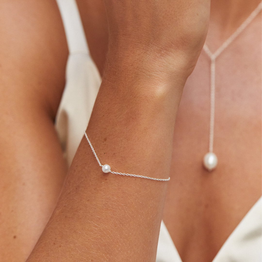 Woman wearing a silver single pearl bracelet on her wrist and silver large pearl lariat necklace around her neck 