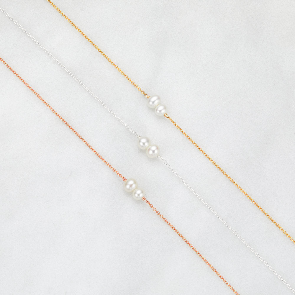 a silver six pearl choker necklace, a gold six pearl choker necklace and a rose gold six pearl choker necklace  next to one another on a marble surface