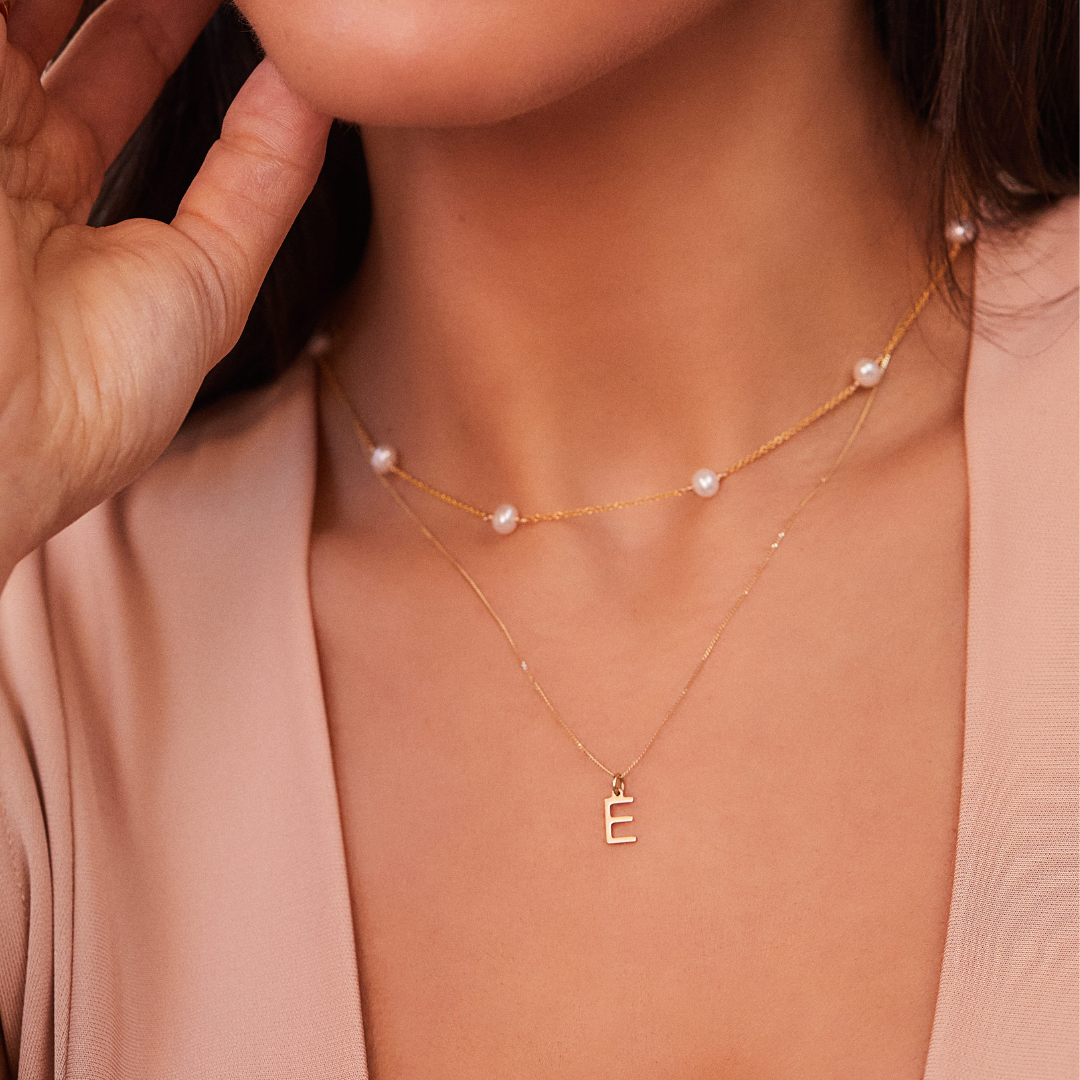 Gold ten pearl choker around a neck pared with a gold chain necklace with a solid gold individual initial charm 'E'
