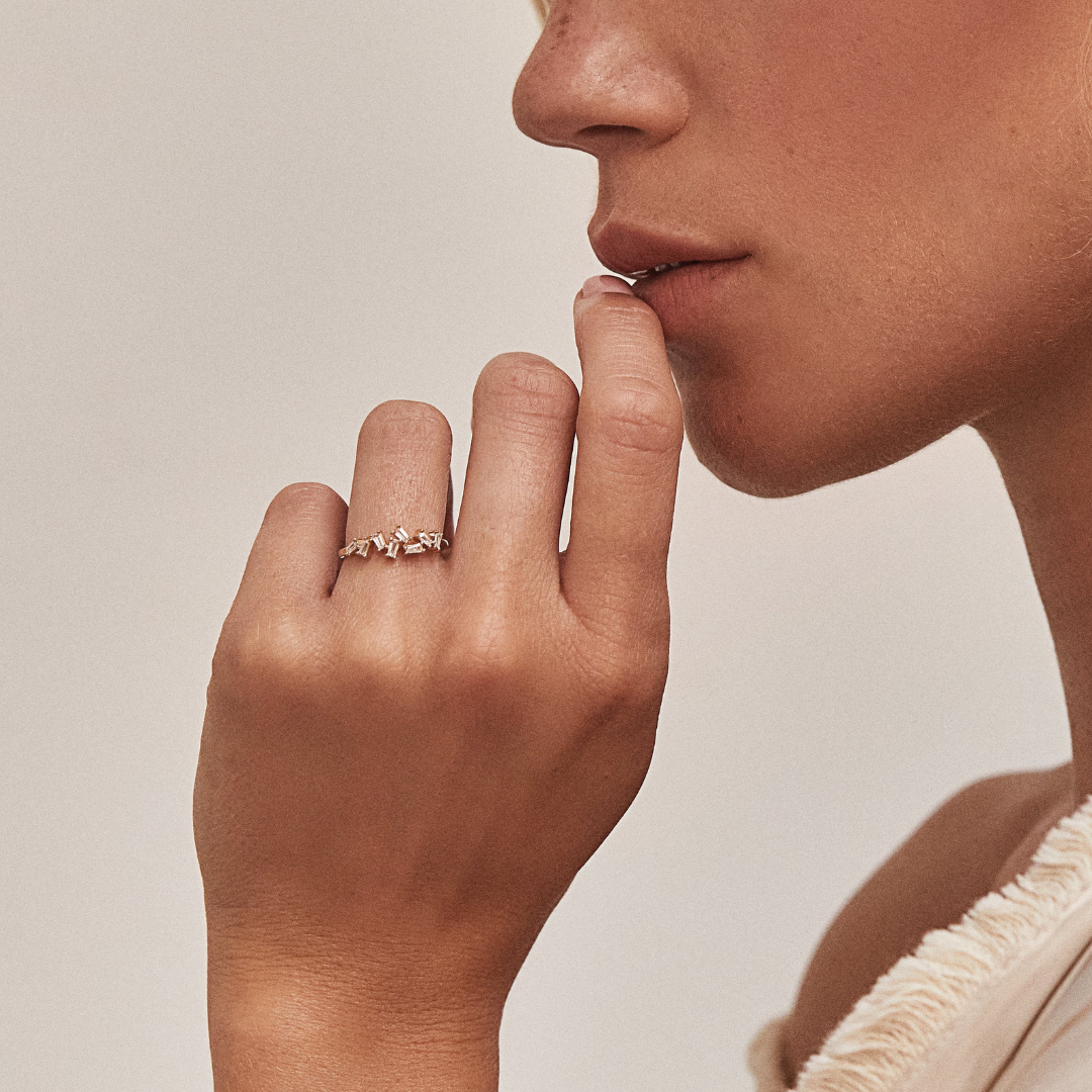 A woman wearing a gold diamond style baguette ring on her finger with her finger to her lips
