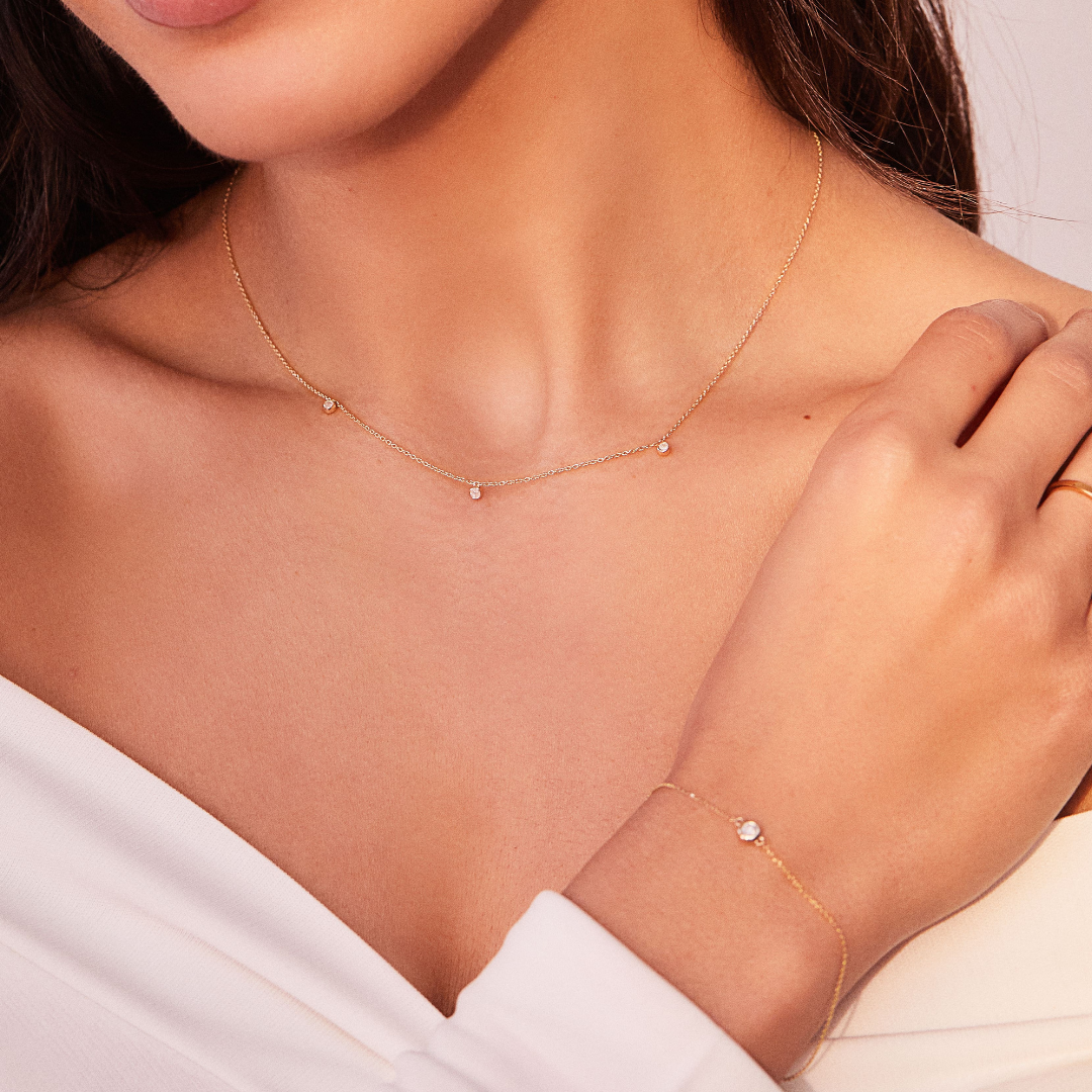 Solid gold diamond drop necklace around a neck of a woman wearing a solid gold diamond bracelet on her wrist