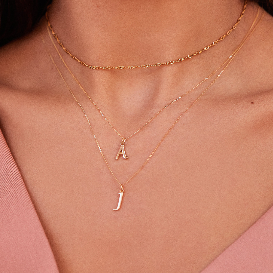 A gold curve initial letter necklace 'A' layered with a gold curve initial letter necklace 'J' and a gold twisted rope choker