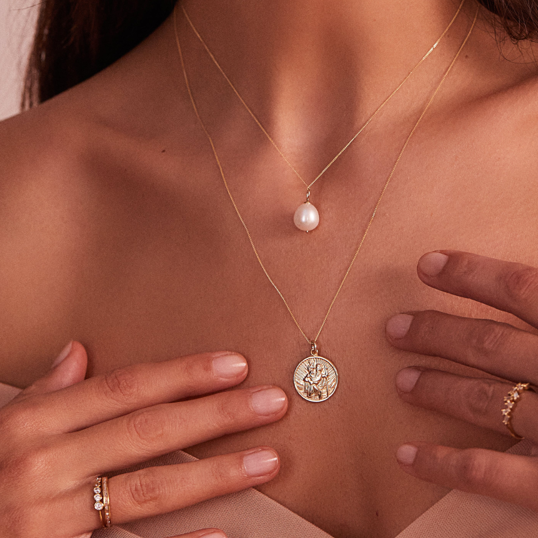 Gold large single pearl necklace around the neck of a woman wearing a gold diamond style eternity ring on her finger