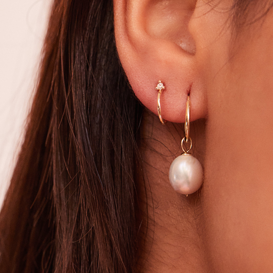 Close up of a solid gold large pearl drop hoop earring and gold diamond style lobe hoop stud earring in an earlobe 