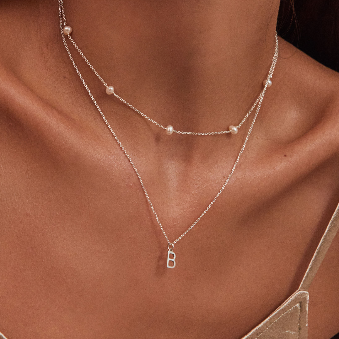Silver ten pearl choker layered with a silver chain with a silver individual initial charm 'B' around a neck