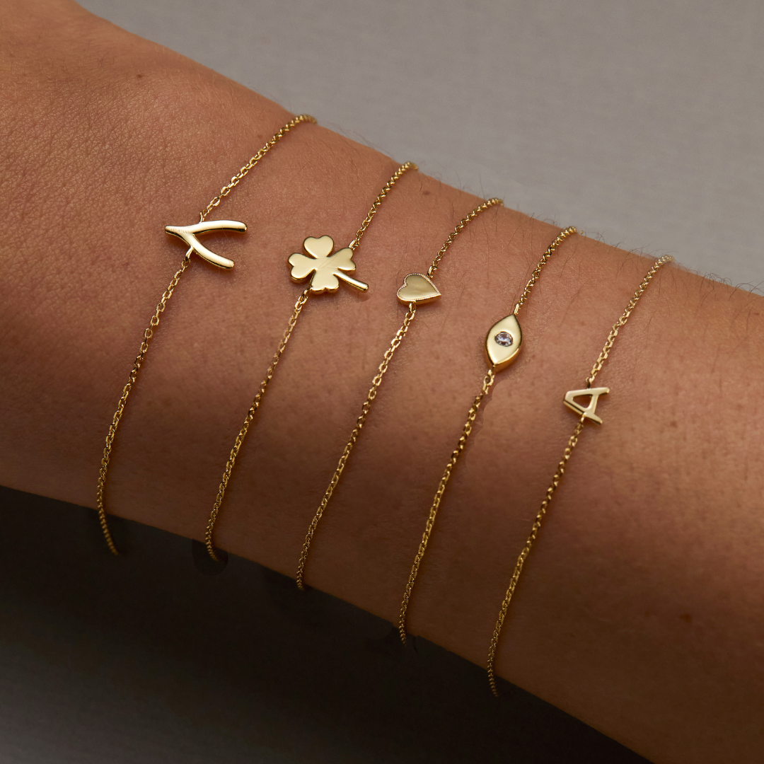 Gold tiny heart bracelet on a wrist worn with other gold tiny bracelets of different shapes