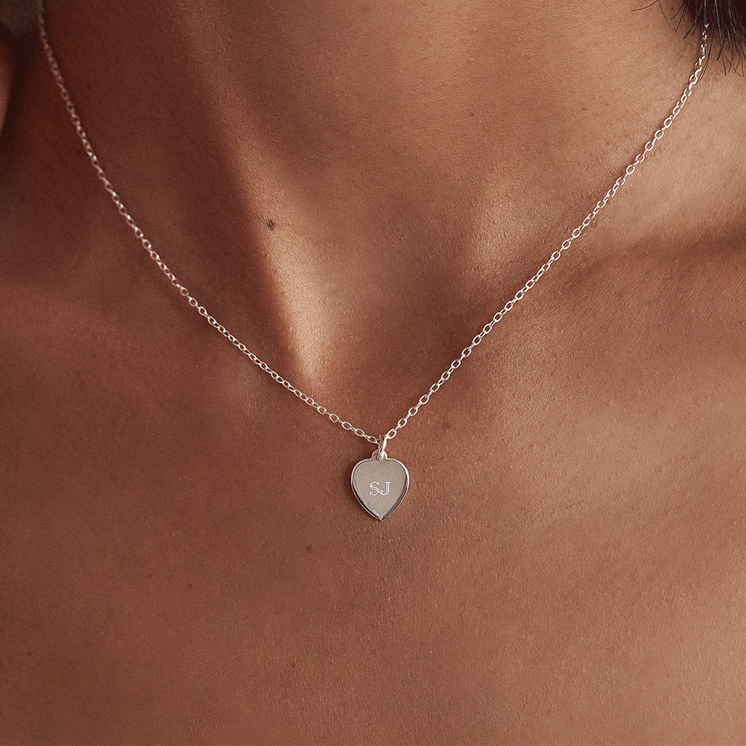 Other side of silver small heart st christopher necklace around a neck with the initials 'SJ' engraved 