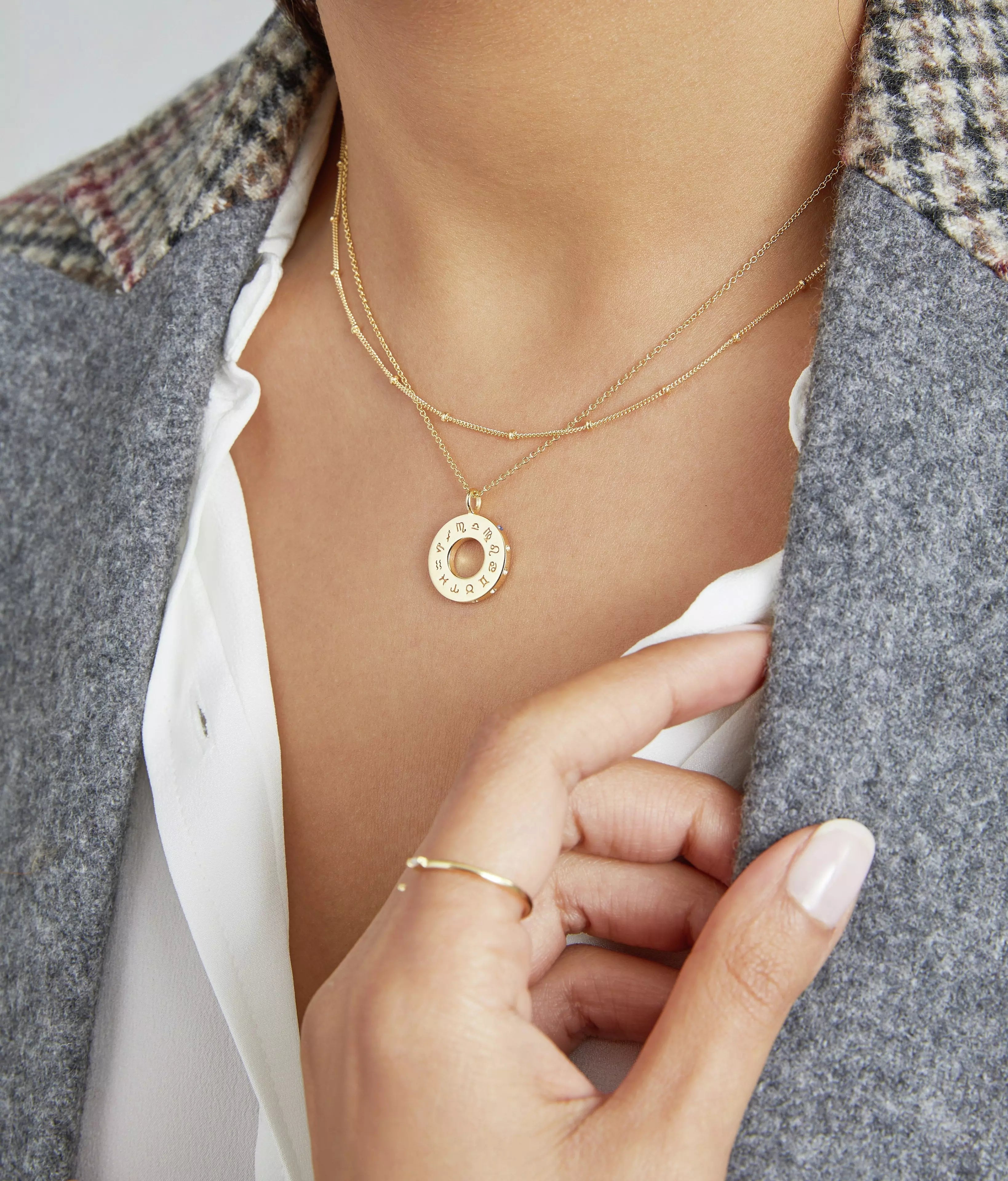 Gold zodiac birthstone necklace on a chest of a woman wearing a grey jacket
