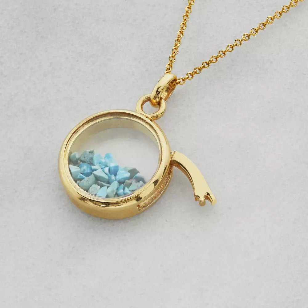 Gold glass gemstone locket with blue gemstones with the side lid open on a grey background