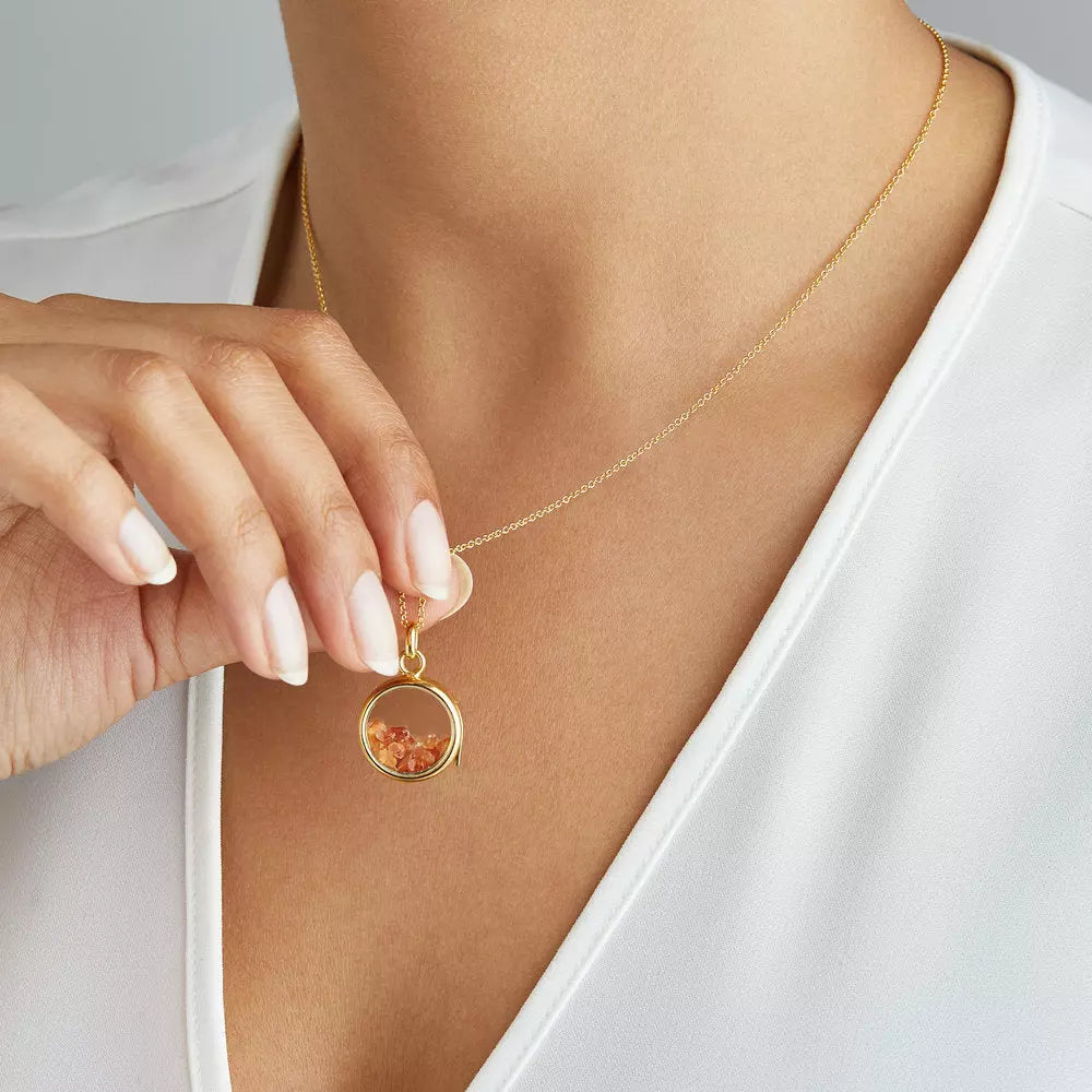Gold glass gemstone locket with transparent white and red gemstones around a neck, held up off the chest by her fingers