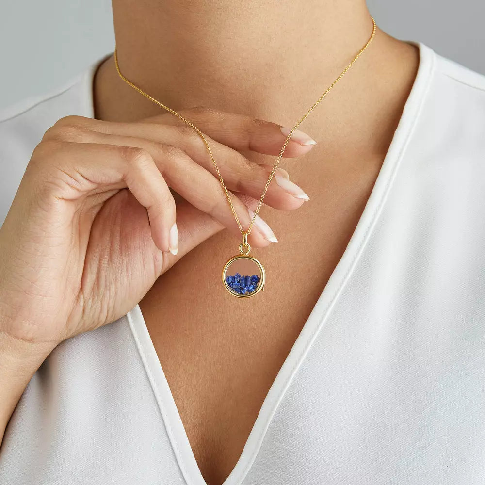 Gold glass gemstone locket with deep blue gemstones around a neck lifted off the chest with her hand