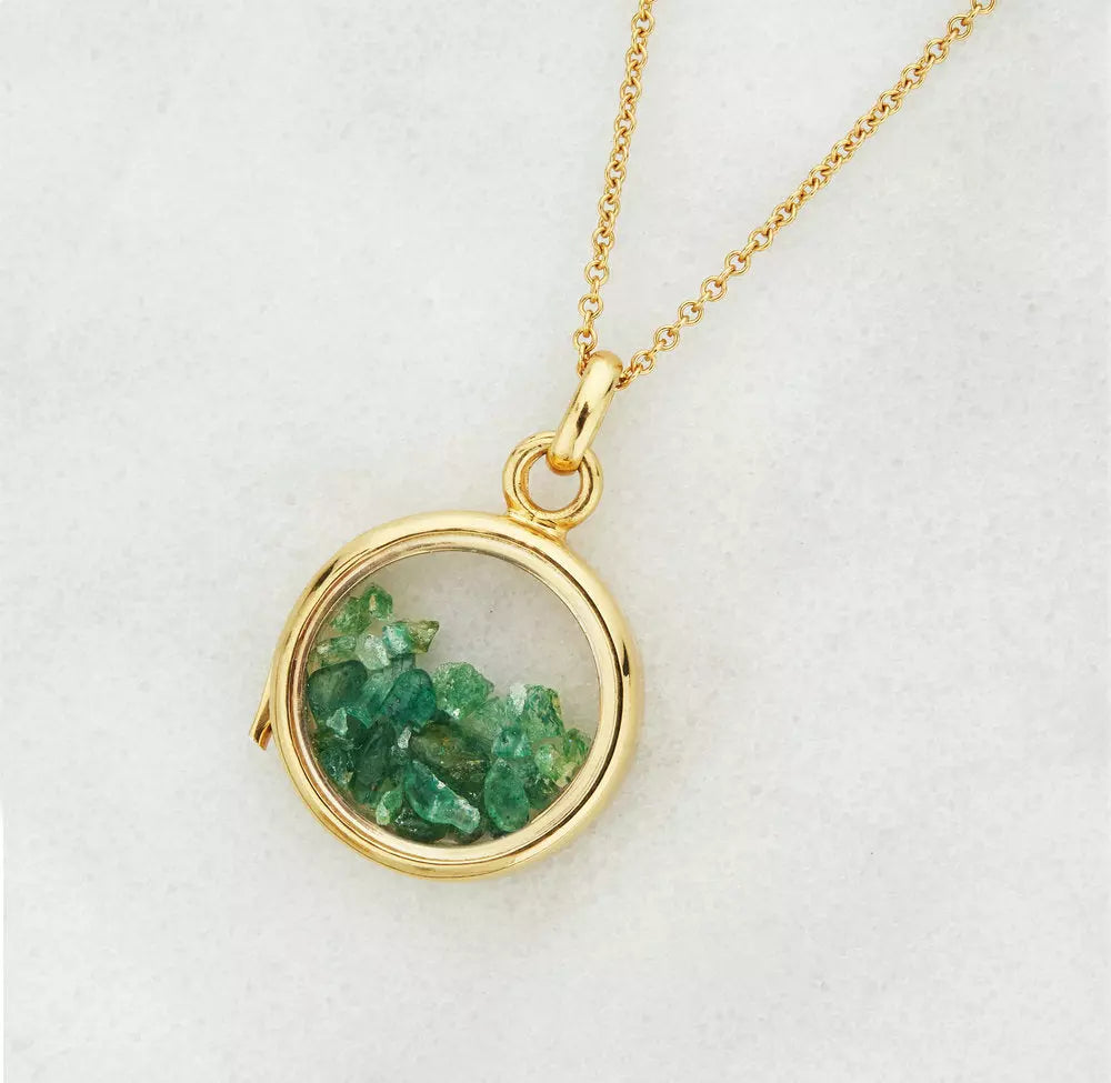 Gold glass gemstone locket with green gemstones on a grey background