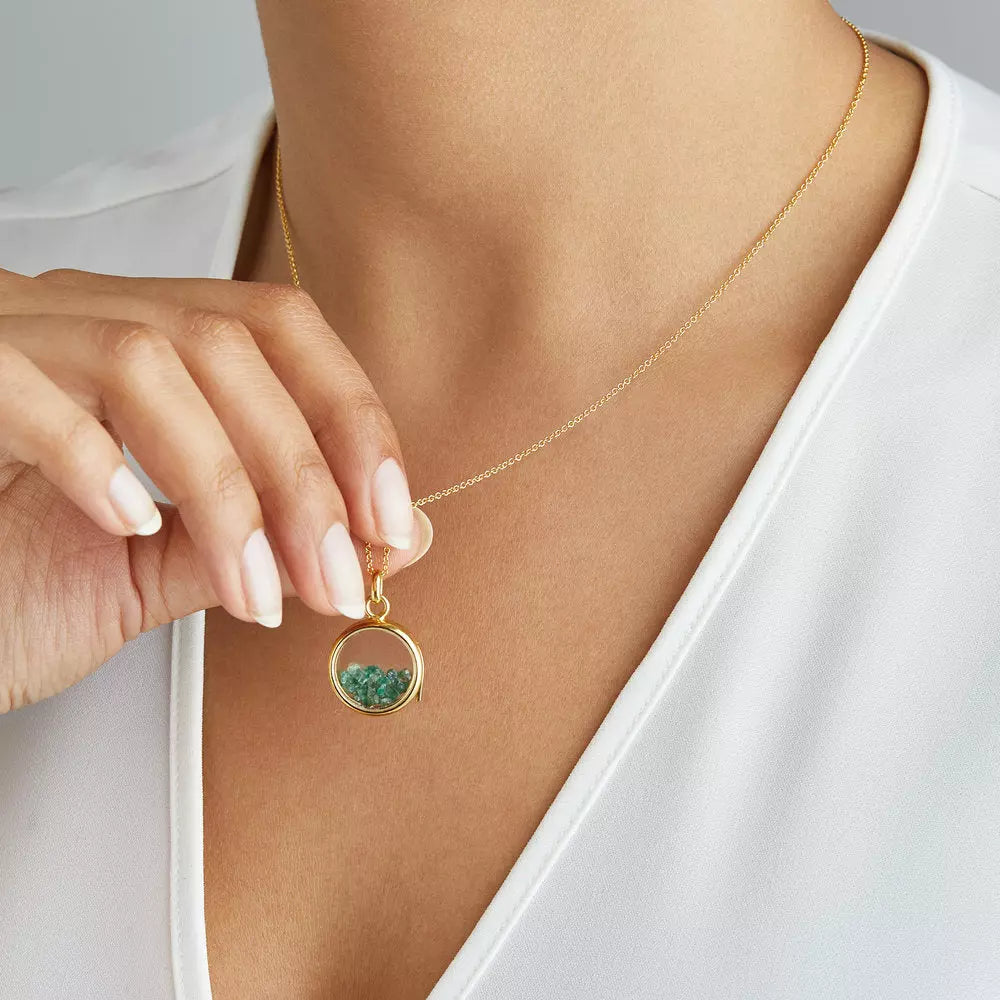 Gold glass gemstone locket with green gemstones around a neck lifted up off the chest with her fingers