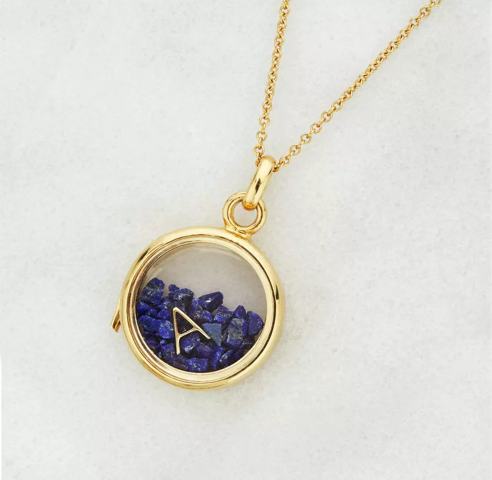 Gold glass gemstone locket with deep blue gemstones and a gold letter A on  a grey background