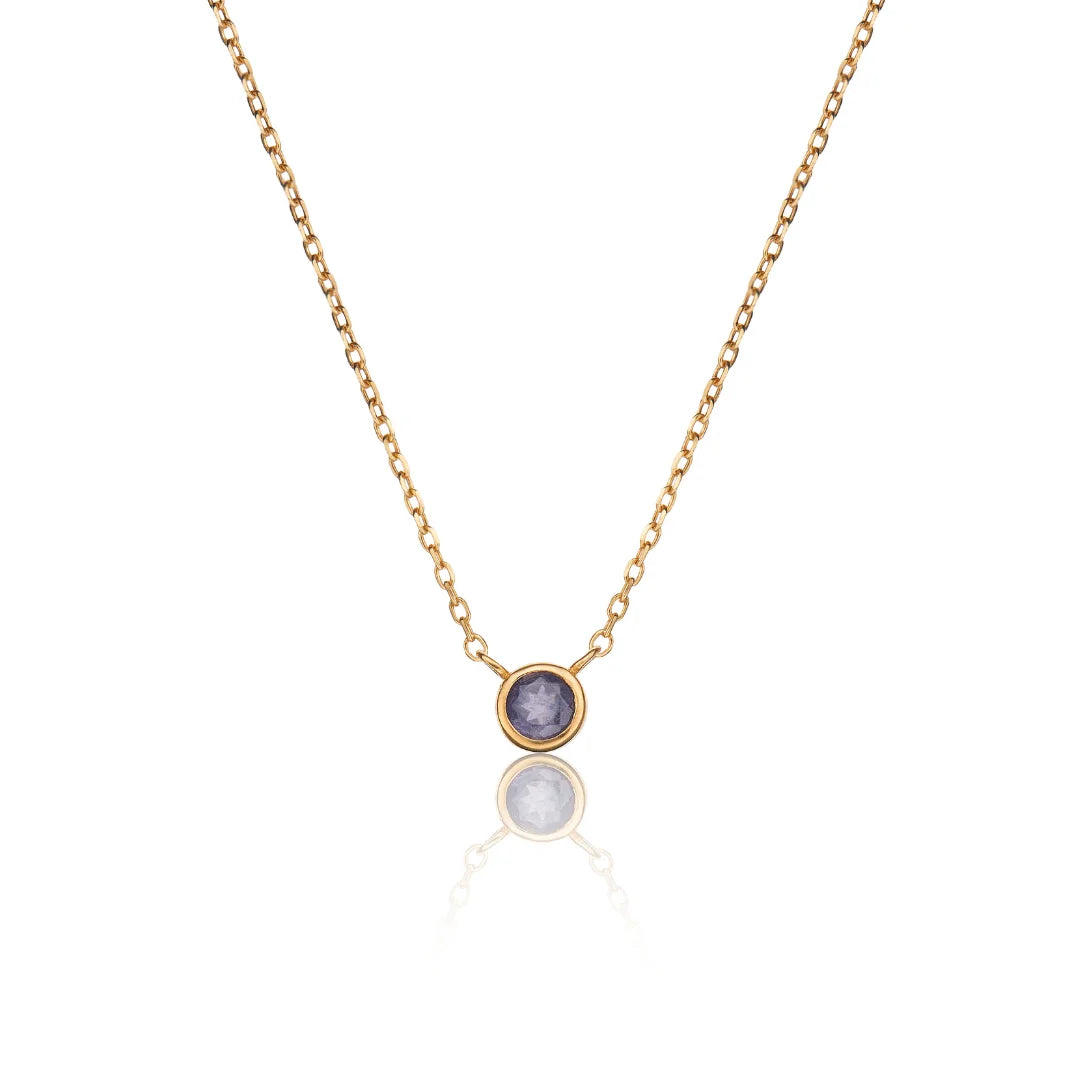 A delicate gold chain necklace featuring a small bezel-set oval pendant with a lavender-purple stone, displayed against a clean white background with a soft reflection below.