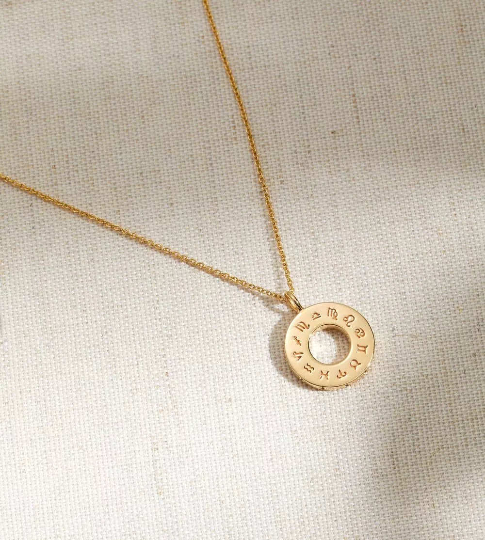 Gold zodiac birthstone necklace on a woven textile surface
