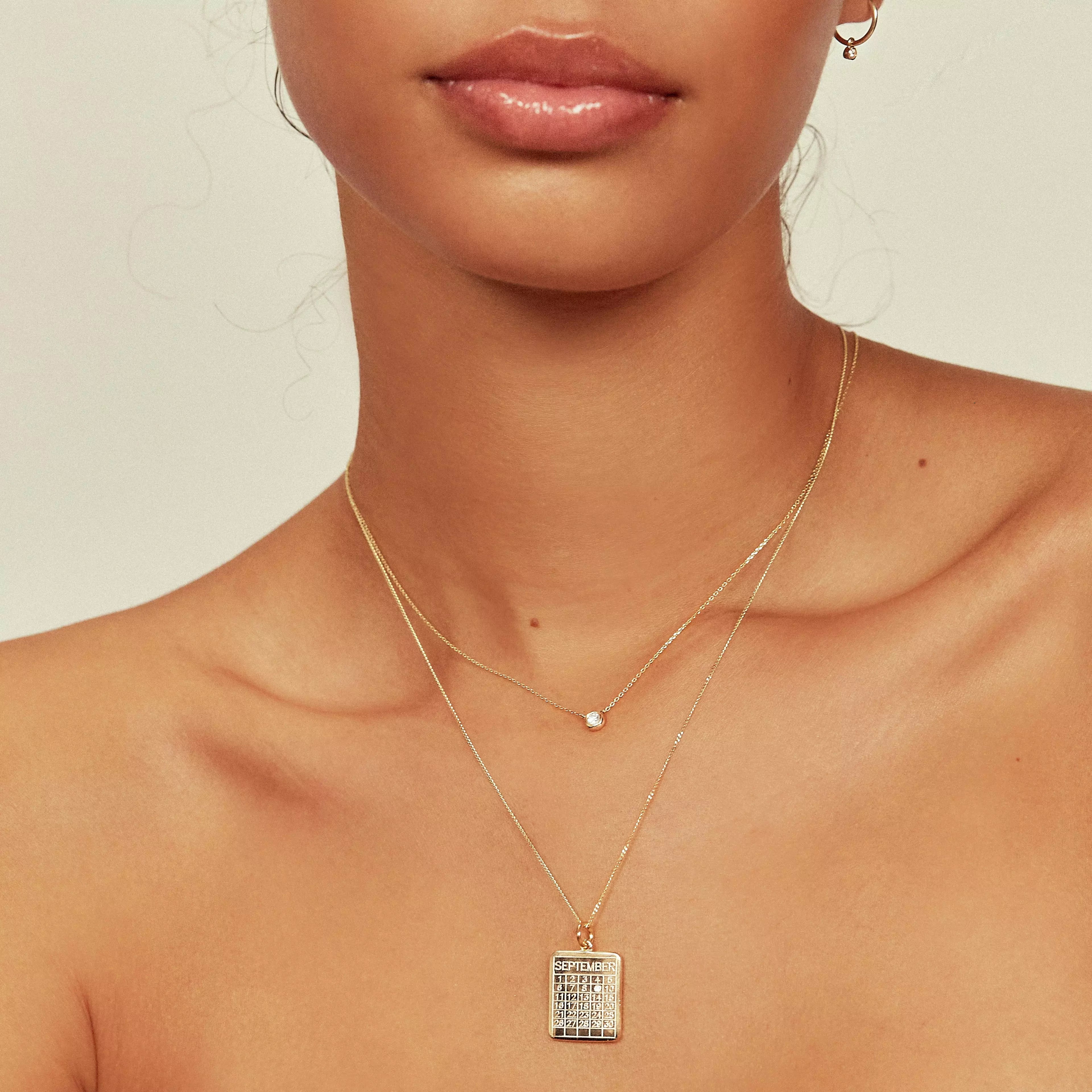 Gold special date calendar necklace 'September' with the gemstone on number '9', layered with a gold single pearl choker around the neck of a woman 